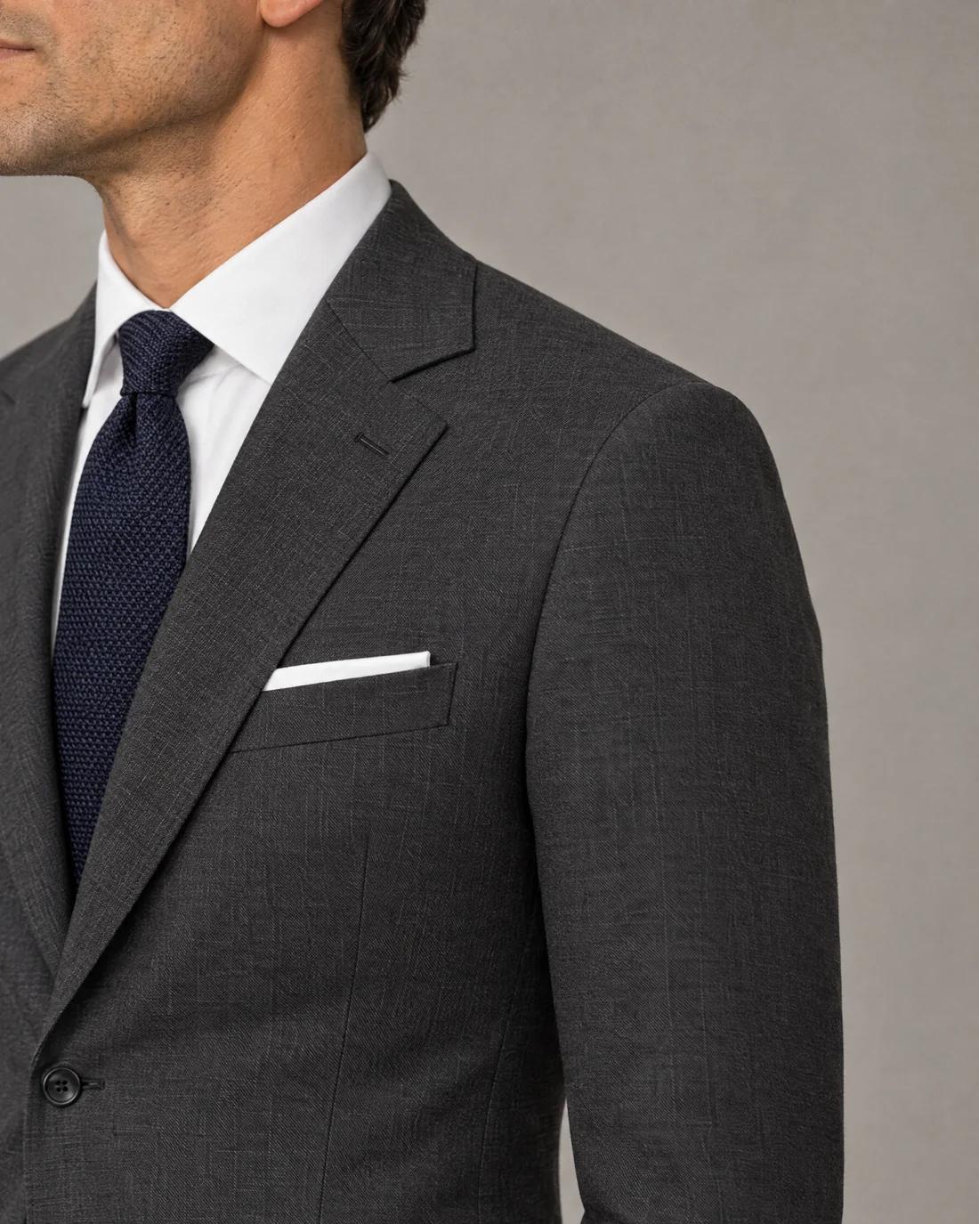 The charcoal shoulder seen close, the seam ending on the bone, the collar against the shirt.