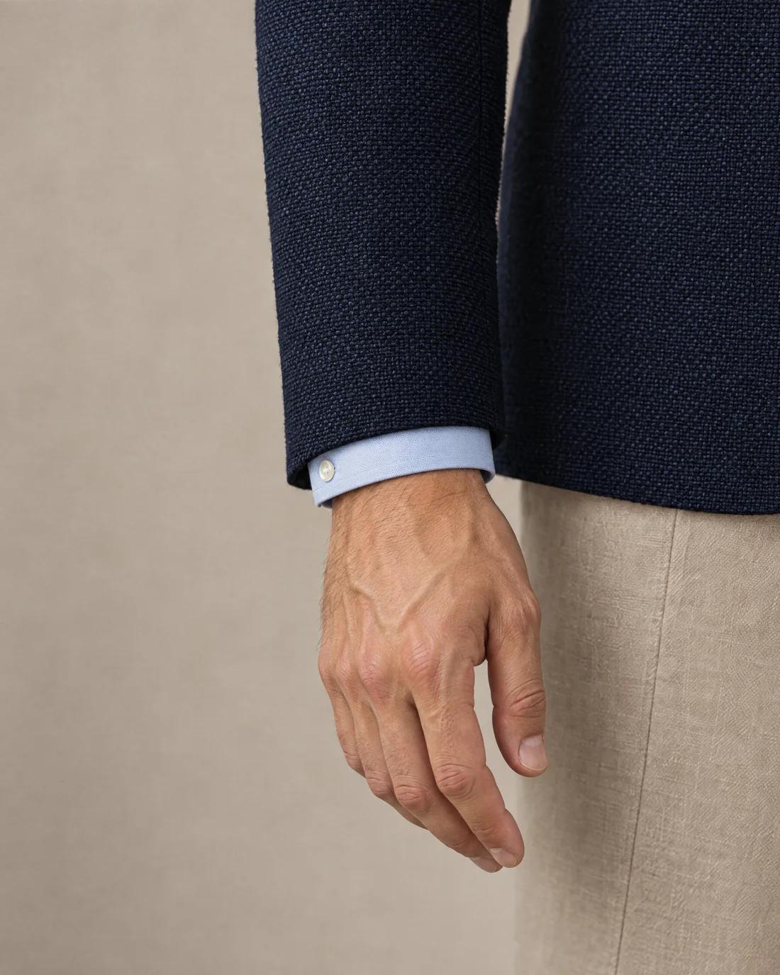 A navy hopsack sleeve ending at the wrist bone, a sliver of pale blue Oxford cuff below it.