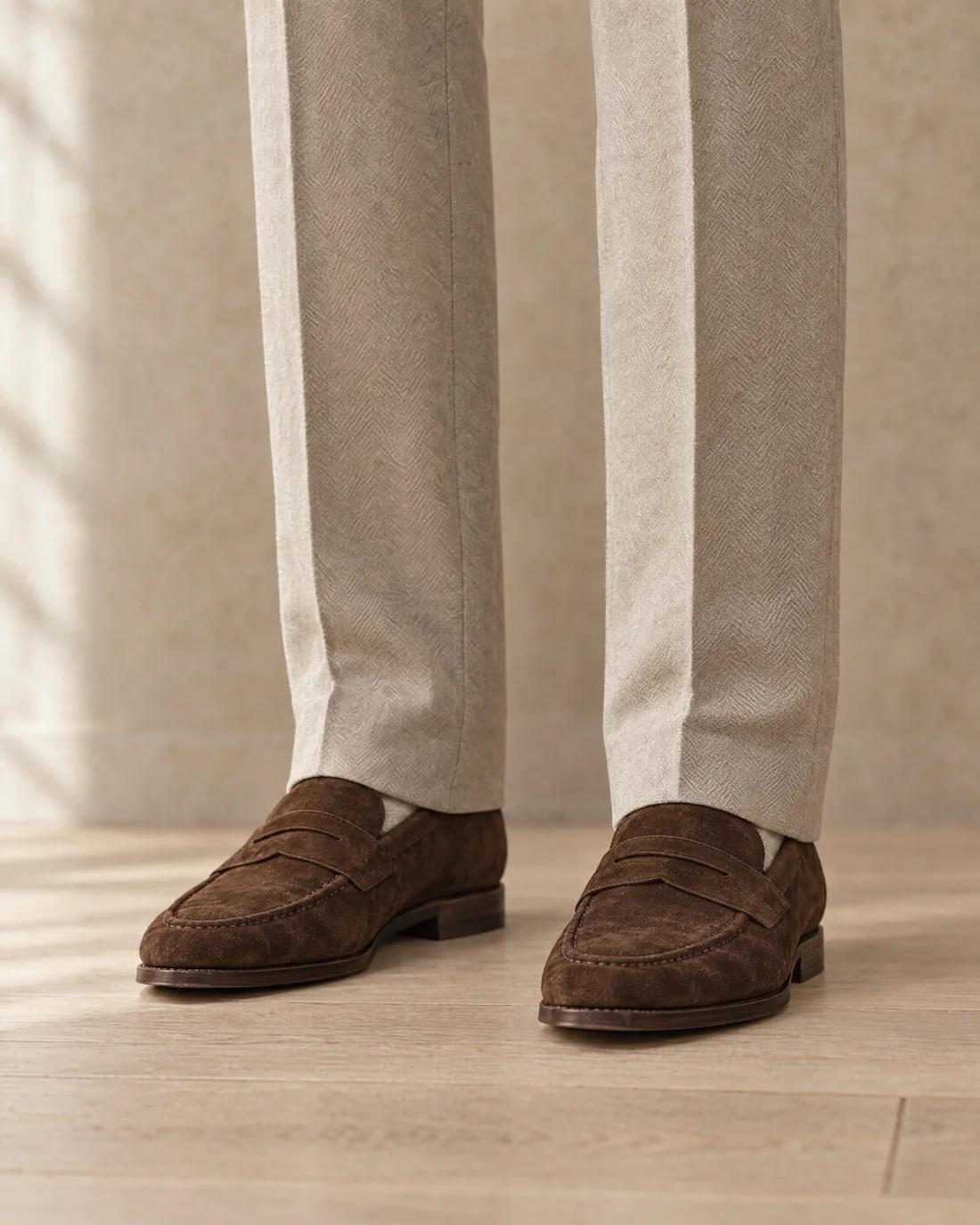 Stone wool trousers resting on brown suede penny loafers with one soft break.